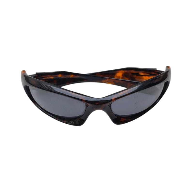 Puede incluir: Gafas de sol deportivas con lente gris oscuro y montura carey marr&oacute;n. Las gafas de sol tienen un dise&ntilde;o curvo y est&aacute;n sobre un fondo blanco. La montura tiene un acabado brillante.