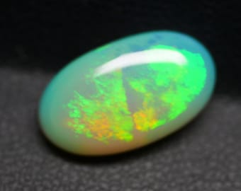 Puede incluir: Una piedra preciosa de ópalo ovalada de color verde claro con un destello verde y naranja brillante.