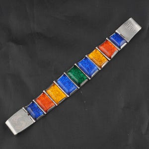 May include: A colorful bracelet with rectangular enamel segments in red, orange, yellow, green, and blue. The bracelet has a silver-toned metal frame and clasp. The clasp is engraved with the initials "ABO".