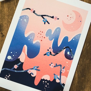 Puede incluir: Una impresión con un diseño de paisaje estilizado en tonos rosa y azul. La obra de arte representa una luna creciente, ramas florecidas y formas abstractas. La impresión está sobre papel blanco, con un fondo de madera.