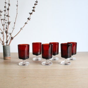 Peut inclure: Ensemble de six verres à liqueur à pied en verre rouge sur une surface en bois.