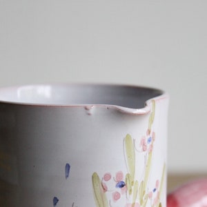 May include: White ceramic jug with a floral design in pink, green and blue. The jug has a slightly uneven rim.
