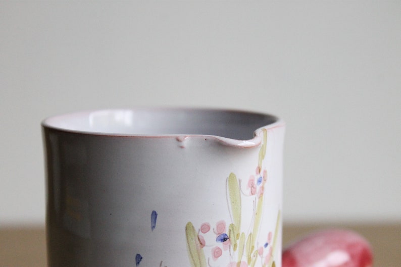 May include: White ceramic jug with a floral design in pink, green and blue. The jug has a slightly uneven rim.