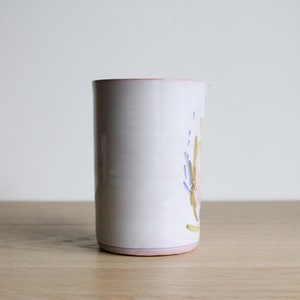 May include: White ceramic vase with a floral design in shades of pink, blue, and green. The vase has a pink rim.
