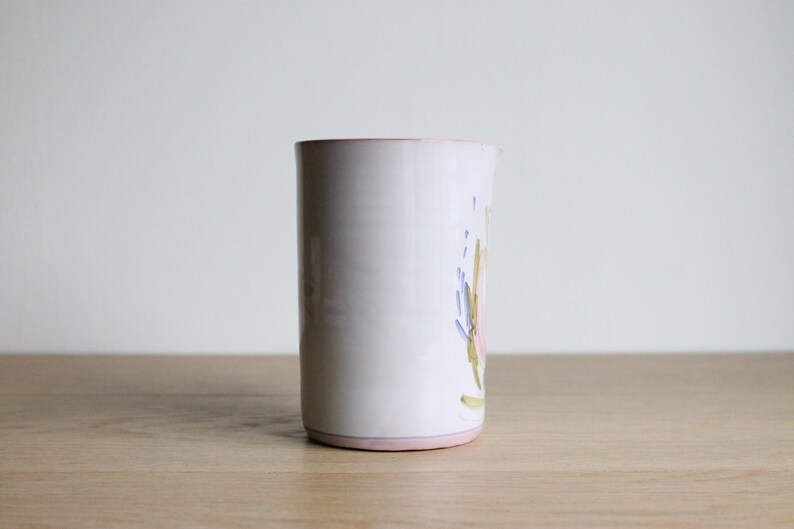 May include: White ceramic vase with a floral design in shades of pink, blue, and green. The vase has a pink rim.