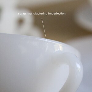 May include: Close-up of a white ceramic mug with a curved handle. The text "a glass manufacturing imperfection" is visible, pointing to a small flaw on the rim. The mug is set against a blurred background.
