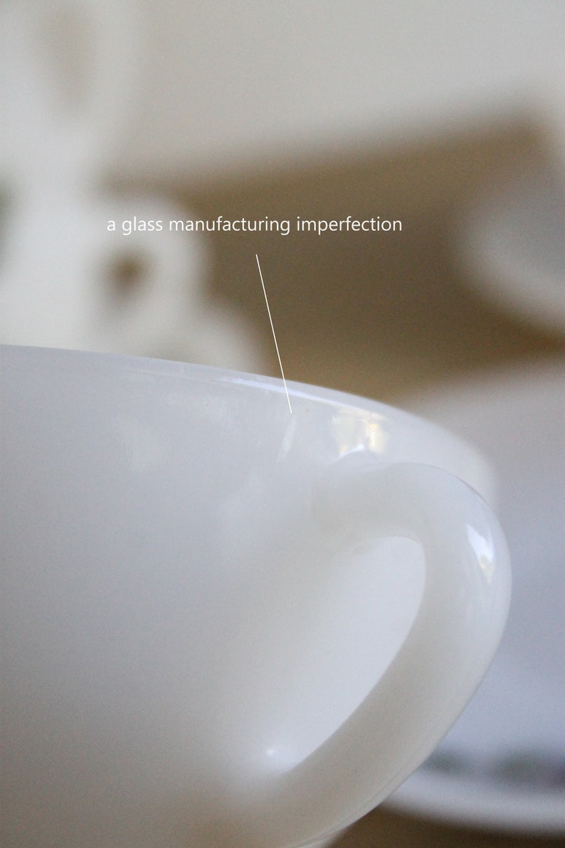 May include: Close-up of a white ceramic mug with a curved handle. The text "a glass manufacturing imperfection" is visible, pointing to a small flaw on the rim. The mug is set against a blurred background.