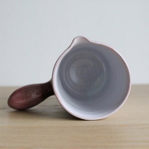 May include: A white ceramic jug with a pink handle. The jug is empty and the inside is visible.
