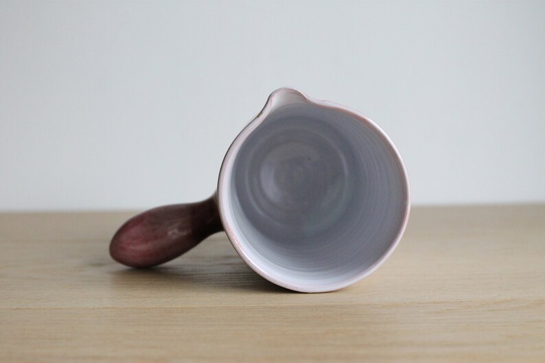 May include: A white ceramic jug with a pink handle. The jug is empty and the inside is visible.