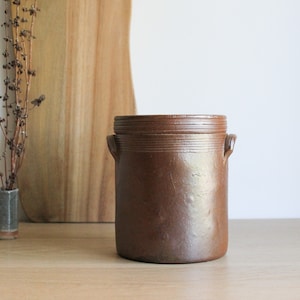 Peut inclure: Un pot en céramique brun avec un couvercle et deux poignées. Le pot est verni et a un aspect rustique.