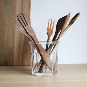 May include: A clear glass jar with a ribbed design holds a collection of wooden kitchen utensils, including a spoon, a spatula, and two forks.
