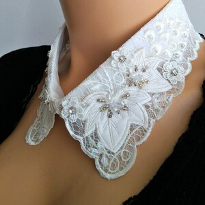 May include: White lace collar with a scalloped edge and embellished with rhinestones and pearls.