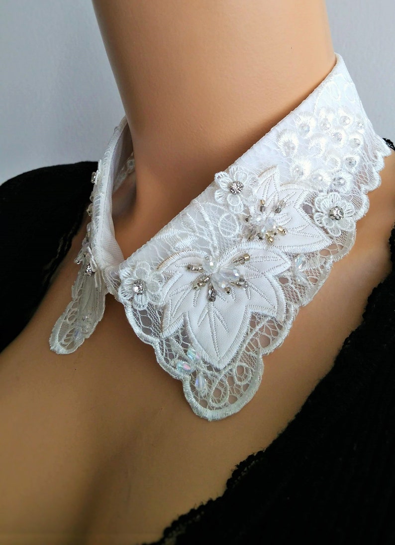 May include: White lace collar with a scalloped edge and embellished with rhinestones and pearls.