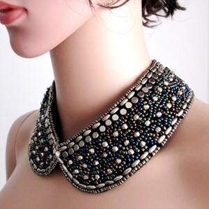 May include: A silver and black beaded collar necklace with a peter pan style collar. The necklace is made of small round beads and larger oval beads.