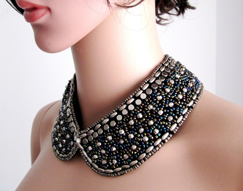 May include: A silver and black beaded collar necklace with a peter pan style collar. The necklace is made of small round beads and larger oval beads.