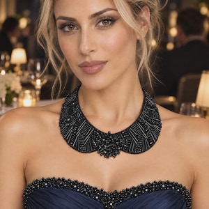 May include: A black beaded collar necklace featuring intricate patterns of small cylindrical and round beads. The necklace is worn over a dark blue strapless dress that has a matching black beaded trim along the top edge of the bodice.
