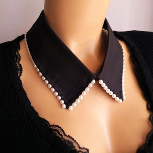 May include: A black fabric collar with a row of white pearl beads around the edge.