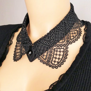 May include: A black lace collar with a button closure. The collar is made of delicate, intricate lace and has a scalloped edge.