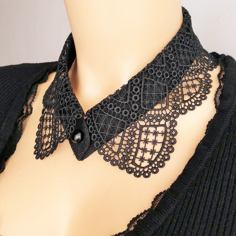 May include: A black lace collar with a button closure. The collar is made of delicate, intricate lace and has a scalloped edge.