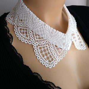 May include: White lace collar with a scalloped edge. The collar is made of delicate lace and is perfect for adding a touch of elegance to any outfit.