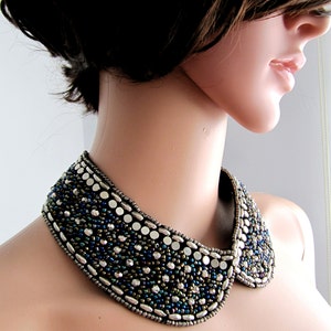 May include: A beaded collar necklace with a wide, rounded shape. The necklace is made of silver, blue, and green beads.