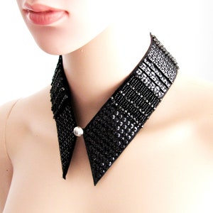 May include: A black sequined collar with a pointed front and a silver button closure. The collar is embellished with rows of small, shiny sequins and beads, creating a textured and glamorous look. The collar is designed to be worn around the neck.