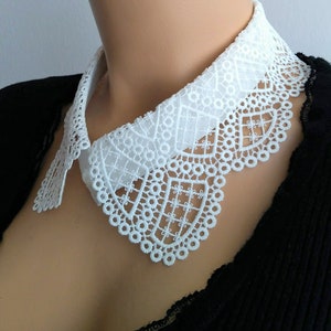 May include: White lace collar with a scalloped edge. The collar is made of delicate lace and has a simple, elegant design.