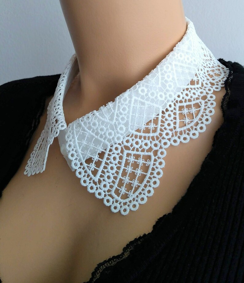 May include: White lace collar with a scalloped edge. The collar is made of delicate lace and has a simple, elegant design.