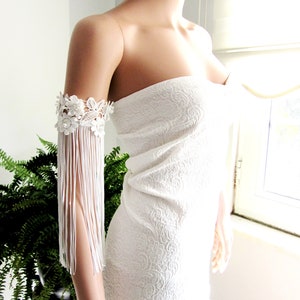 May include: White strapless dress with a white lace and fringe arm cuff.