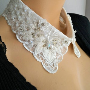 May include: A white lace collar with a scalloped edge and delicate floral designs. The collar is adorned with iridescent crystals and beads.