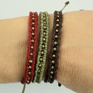 May include: Three braided bracelets with metal beads. The bracelets are red, green, and brown.