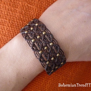 May include: A brown woven bracelet with gold beads. The bracelet is made with a macrame knot pattern.