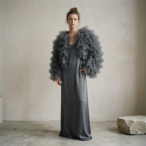 Könnte beinhalten: Ein bodenlanges, anthrazitfarbenes Satin-Slip-Kleid mit V-Ausschnitt und Seitentaschen, kombiniert mit einem passenden Bolero aus anthrazitfarbenem Tüll mit dichten, geschichteten Rüschen an Ärmeln und Schultern.