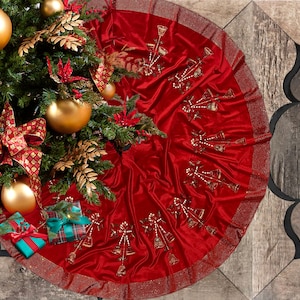 May include: Red velvet Christmas tree skirt with a gold glitter trim and a design of gold bells. The skirt is decorated with gold and white beads.