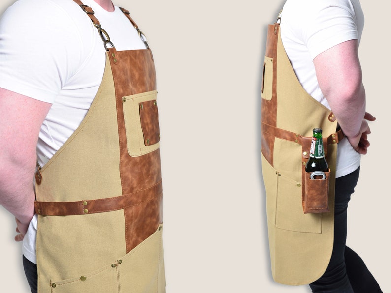 May include: A tan and brown apron with leather accents and multiple pockets. The apron has a built-in bottle opener and a pocket designed to hold a bottle. The apron is designed for use in a kitchen or workshop.