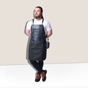 May include: A dark blue and black apron with a leather chest pocket and a side pocket for holding bottles. The apron has adjustable straps and is designed for use in a kitchen or workshop setting.