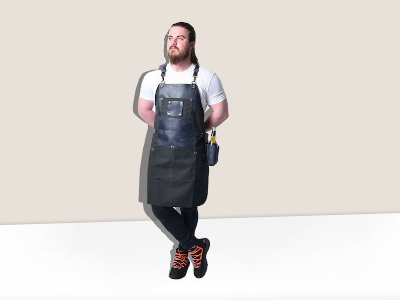 May include: A dark blue and black apron with a leather chest pocket and a side pocket for holding bottles. The apron has adjustable straps and is designed for use in a kitchen or workshop setting.