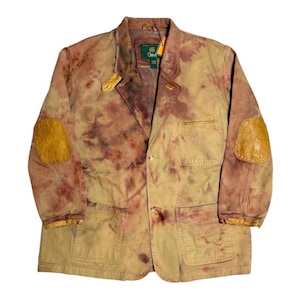 May include: A tan blazer with brown and burgundy tie-dye patterns, featuring leather elbow patches and a notched lapel. The jacket has two front pockets and a button closure. The tag reads "Orvis".