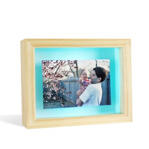 May include: A wooden picture frame with a light blue background and a photo of a father holding a young child in front of a flowering tree.