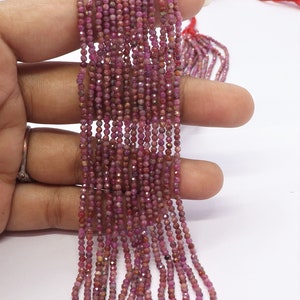 May include: A strand of pink ruby beads, faceted and strung on a thread. The beads are small and uniform in size, and the strand is long enough to be used for jewelry making or other crafting projects.