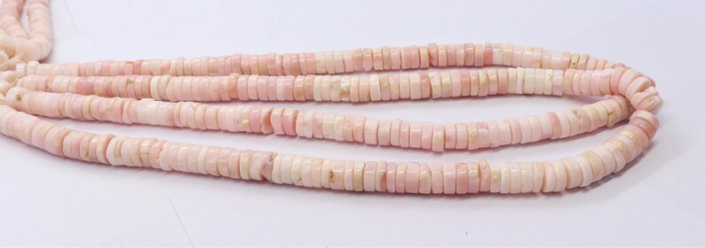 Pode incluir: Close-up de fios de contas planas em forma de disco, rosa e creme. As contas s&atilde;o enfiadas, criando um efeito em camadas. As contas t&ecirc;m uma apar&ecirc;ncia natural e org&acirc;nica, com varia&ccedil;&otilde;es de cor e textura.