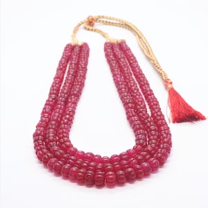 Puede incluir: Un collar de múltiples hilos hecho de cuentas de rubí rojo oscuro. El collar está encordado en un cordón dorado con una borla roja.