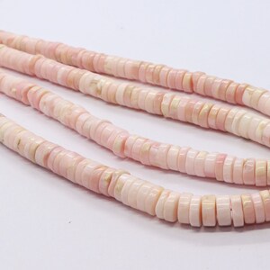Pode incluir: Close-up de v&aacute;rios fios de contas rosa e brancas em forma de disco. As contas s&atilde;o planas, circulares e t&ecirc;m uma superf&iacute;cie ligeiramente irregular. A cor &eacute; um rosa pastel suave com detalhes brancos.