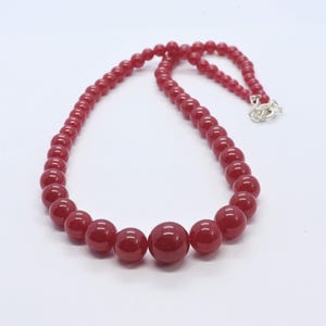 May include: A red beaded necklace with a larger red bead in the center.