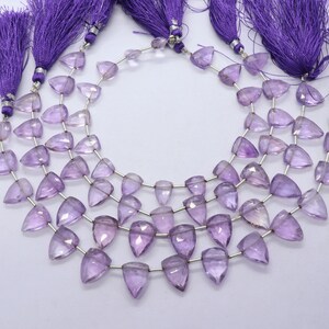 May include: A strand of amethyst gemstone beads, each bead is faceted and shaped like a triangle. The beads are strung on silver wire and have a purple hue. The strand is finished with purple tassels.