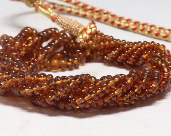 May include: A strand of amber-colored glass beads, strung together to form a necklace. The beads are round and have a smooth, polished finish.