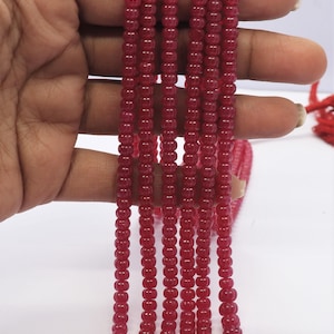 May include: A strand of red gemstone beads. The beads are round and have a smooth, polished finish. The strand is approximately 18 inches long.