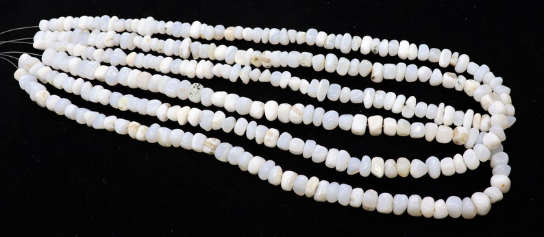 May include: A strand of white gemstone beads, with a smooth, irregular shape. The beads are strung on a clear thread and are arranged in a loose, flowing pattern.
