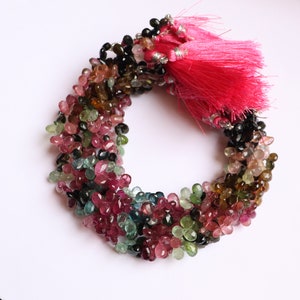 Puede incluir: Una hebra de cuentas de piedras preciosas multicolores, incluyendo rosa, verde, azul y negro, con un borla rosa en el extremo.