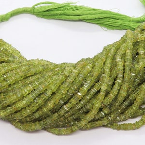 Könnte beinhalten: Eine Strähne grüner Peridot-Perlen, jede Perle ist quadratisch und facettiert. Die Perlen sind auf einem grünen Faden aufgefädelt und bereit für die Schmuckherstellung.